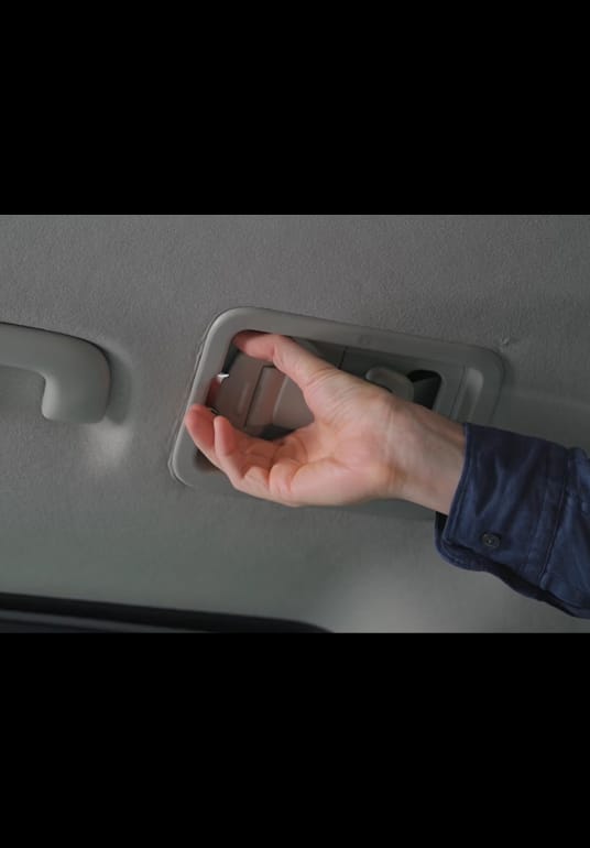 Eine Person hilft dabei, den 3-Punkt-Sicherheitsgurt bei einem Rollstuhlfahrer im Kia PV5 WAV anzulegen.